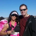 A woman holding a medal stands next to a man. Both are wearing sunglasses and smiling, exuding joy like creating and reaching new milestones. The background shows blue sky and a few people.
