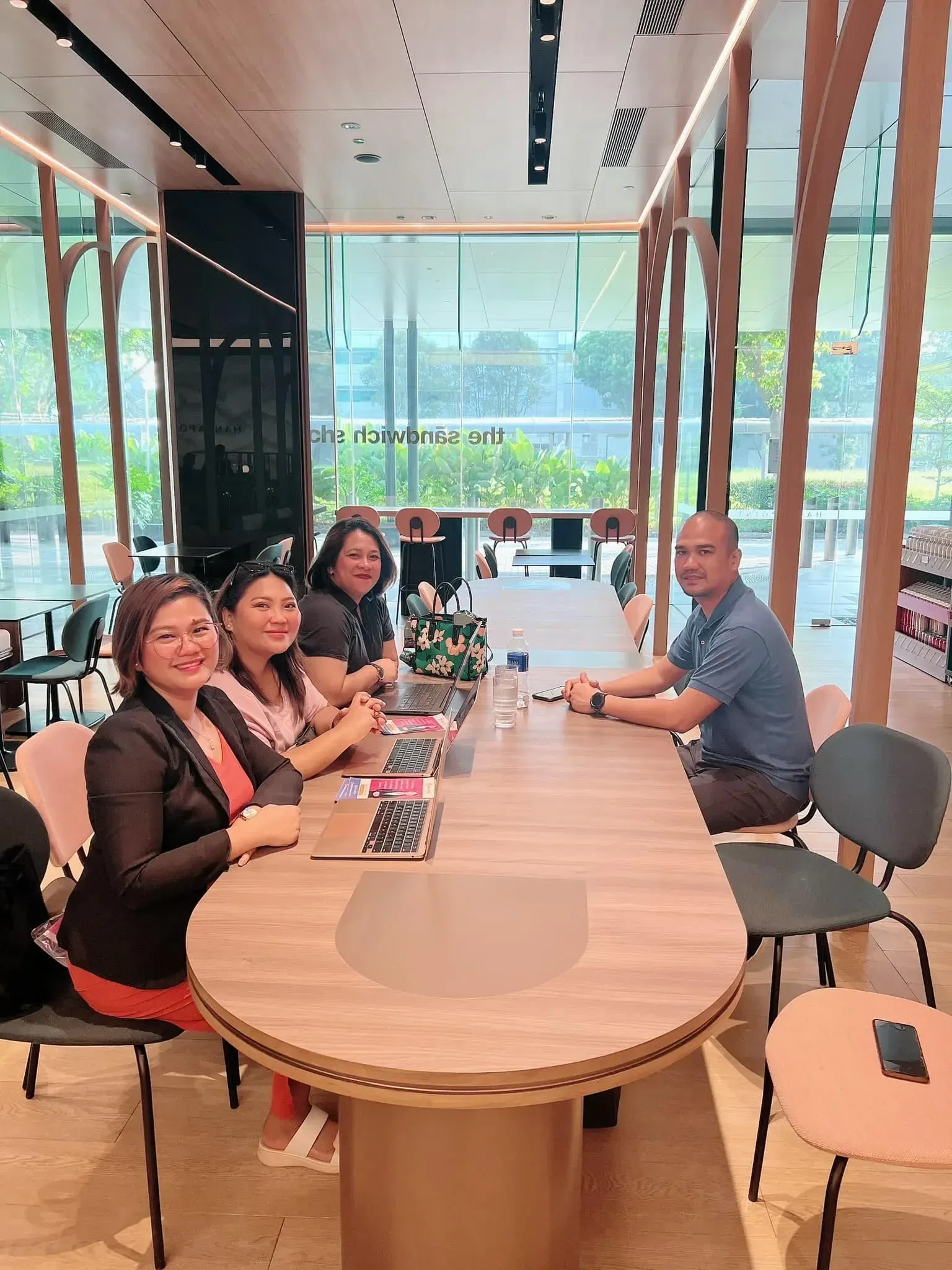 Four people sitting at a table in a modern cafe, laptops and notebooks spread before them, engaging in lively discussion about how Virtual Assistant Philippines empowers businesses. They're strategizing to Create and Reach VA solutions that elevate productivity and efficiency.