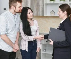 A couple shakes hands with a professional woman holding a folder in a modern office setting, discussing staff management strategies to enhance business security.