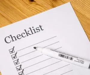 A checklist with several items marked completed, placed on a wooden surface, subtly highlights client retention strategies in progress, with a white marker lying on it.