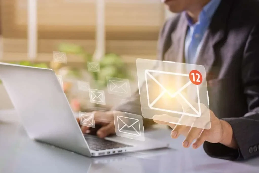 A person in a suit using a laptop, touching a virtual envelope icon showing 12 new email notifications.